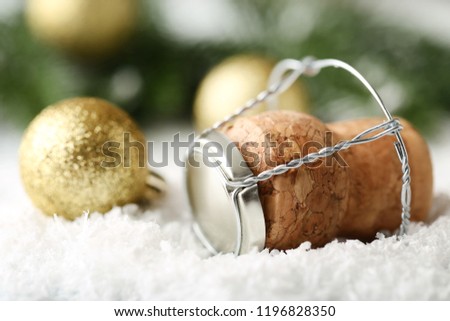 Champagne cork with cap and golden bauble on white snow