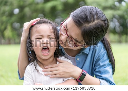 Asian attractive smart mother comforting her daughter after getting hurt from playing on grass fields in the park. Crying cute asian child with her parent. family and kid concept.