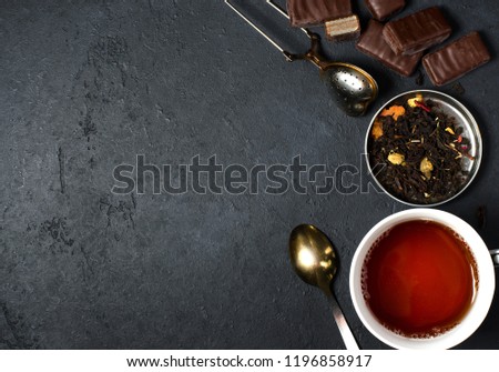 Chocolates and black tea with herbs. Metal tea strainer, spoon. Dark background. Copy space. Flat lay