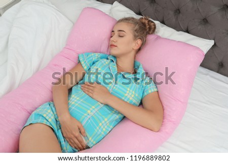 Beautiful pregnant woman sleeping with maternity pillow on bed at home