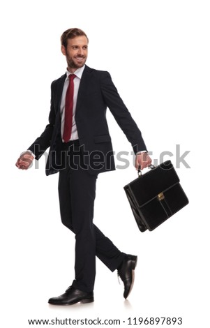 side view of happy businessman holding briefcase walking on white background and looking to side, full length picture