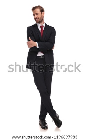 confident businessman stands cross-legged on white background and looks down to side, full length picture