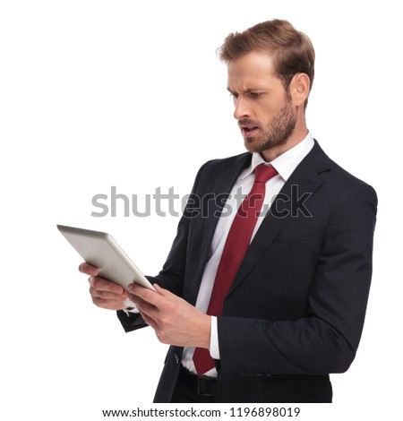 side view of shocked businessman wearing red tie and navy suit reading from his pad while standing on white background, portrait picture