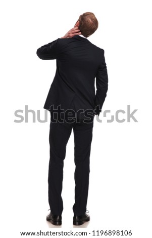 rear view of pensive businessman looking up to side while standing on white background with hands in pockets, full length picture