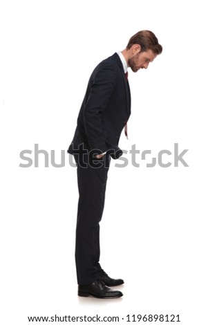 side view of relaxed businessman looking down while standing on white background with hands in pockets, full body picture