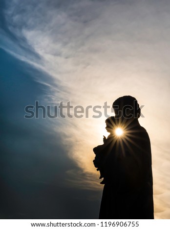 Silhouette of mother (Mary) holding baby child (Jesus) with sunburst rays of light between them