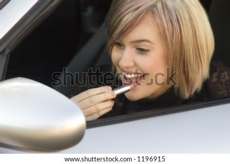 cute blond teen putting lipstick on using car mirror