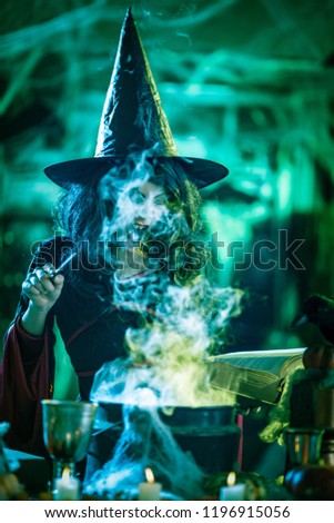 Witch with awfully face reading recipes of magic drink in creepy surroundings and smoky background.