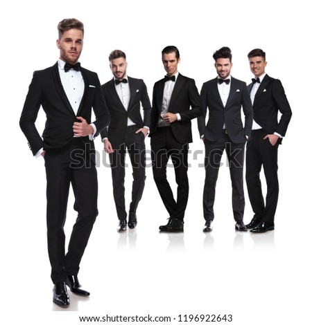 team of five groomsmen in tuxedoes standing on white background with leader in front, full body picture