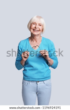 Fashionable senior female. Beautiful senior woman looking at camera and smiling while standing against grey background