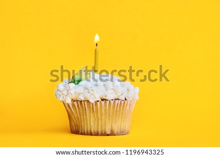 Pretty lemon flavored cupcake with buttercream frosting and decorated with white chocolate shavings and one candle burning. Free space for copy text over a fun yellow background.