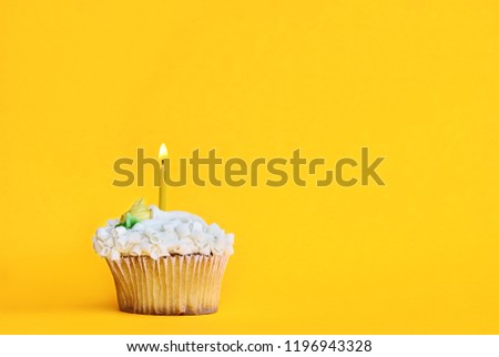 Pretty  lemon flavored cupcake with buttercream frosting and decorated with white chocolate shavings and one candle burning. Free space for copy text over a fun yellow background.