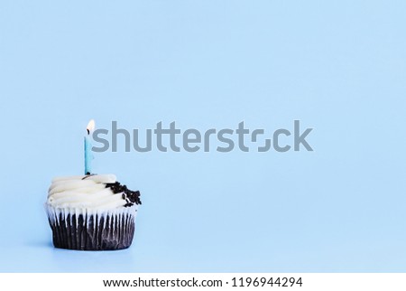 Pretty chocolate flavored cupcake with vanilla buttercream frosting decorated with white chocolate shavings, chocolate chips and one candle burning. Free space for copy text.