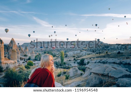girl in ethnic clothes at dawn watching the flight a lot of balloons fly over the valley of love