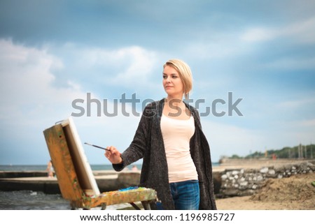 Beautiful young woman painting on the background of the sea and sky. The concept of creativity a beautiful portrait of the painter on outdoor.