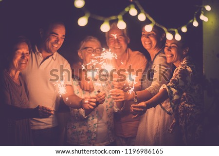 group of caucasian people friends with different ages celebrate together a birthday or new year eve by night outdoor at home. lights and sparkles  with cheerful women and men having fun in friendship Royalty-Free Stock Photo #1196986165