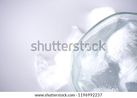 Cold water is in a glass and ice is placed around it. On the white floor. 