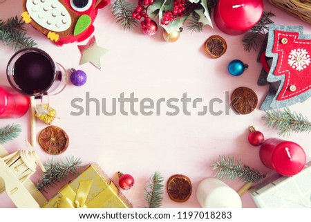 Christmas frame or border with a large assortment of christmas prop, decorations, balls, gifts and candles on a pink wooden background with pine branches and copyspace, overhead view.