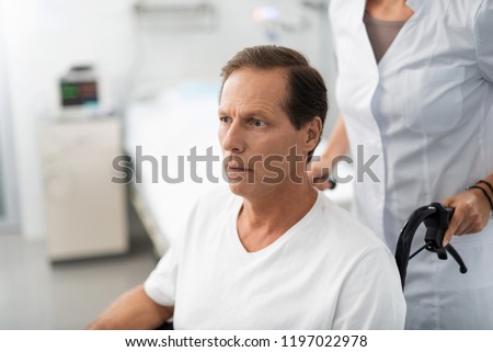 I do not like this. Portrait of paralyzed patient looking away with concerned expression while nurse in in white lab coat standing behind him