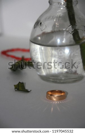 Wedding gold ring on the table. White background with red thread and 
fallen leaves and water bottle. Macro