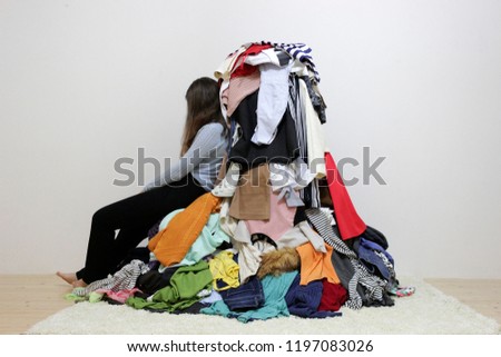 Tired girl sitting near a big oile of differect clothes Royalty-Free Stock Photo #1197083026