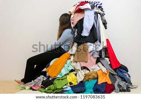 Sad girl sitting near a big pile of differect clothes Royalty-Free Stock Photo #1197083635