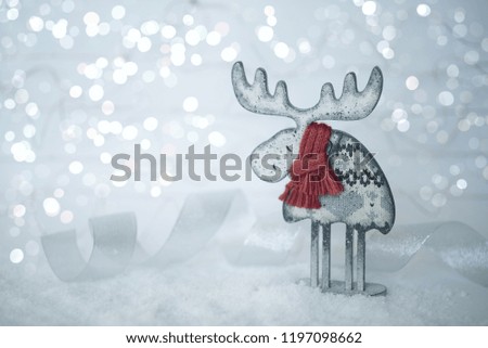 Christmas decoration on abstract twinkling lights background, vintage filter, soft focus. Wooden deer with a red knitted scarf on the snow against a background of blurry lights. Copy space for text.