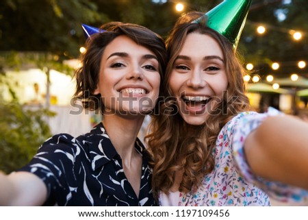 Image of happy young women friends outdoors in park having fun looking camera take a selfie.