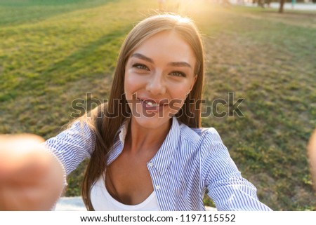 Close up of a cheerful young woman taking a selfie at the park with outstretched hands
