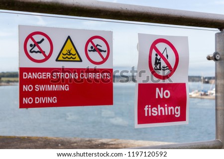 Warning signs on a guardrail/handrail overlooking a river.