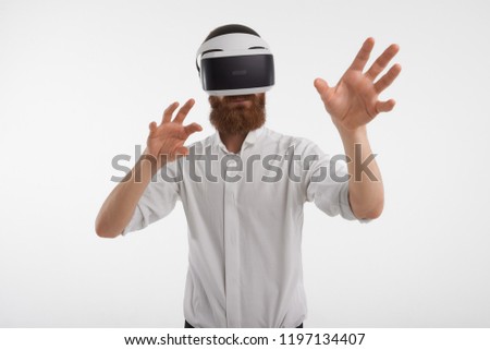 Cyberspace, modern technology and innovations concept. Unrecognizable male with red beard posing in studio wearing white shirt sand oculus goggles, exploring virtual reality, touching something
