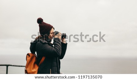 Side view of woman taking photographs of a landscape with her dslr camera. Woman in warm wear stands on top of the mountain and takes pictures of the landscape with her digital camera.