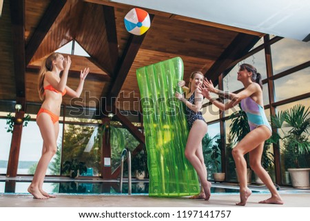 Slim young women playing with a beach ball at indoor swimming pool