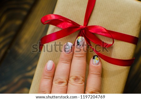 female hand with manicure holds gift box with a bow on a dark wooden background