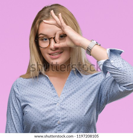 Young caucasian business woman wearing glasses over isolated background doing ok gesture with hand smiling, eye looking through fingers with happy face.