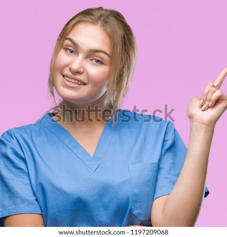 Young caucasian nurse woman wearing surgeon uniform over isolated background with a big smile on face, pointing with hand and finger to the side looking at the camera.