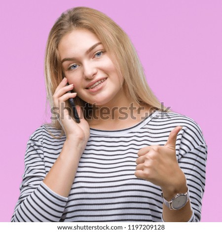 Young caucasian woman showing smartphone screen over isolated background happy with big smile doing ok sign, thumb up with fingers, excellent sign