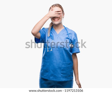 Young blonde surgeon doctor woman over isolated background smiling and laughing with hand on face covering eyes for surprise. Blind concept.