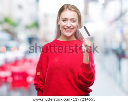Young blonde woman holding credit card over isolated background with a happy face standing and smiling with a confident smile showing teeth
