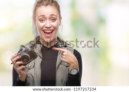 Young blonde woman taking pictures using vintage camera over isolated background very happy pointing with hand and finger