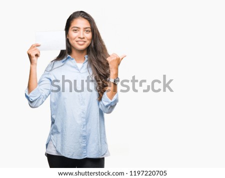 Young arab woman holding blank card over isolated background pointing and showing with thumb up to the side with happy face smiling