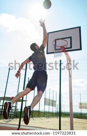 Full length back view portrait of young sportsman shooting slam dunk in basketball court outdoors, copy space