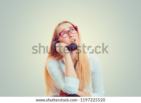 Young blond woman in eyeglasses looking up in boredom and irritation while speaking on telephone