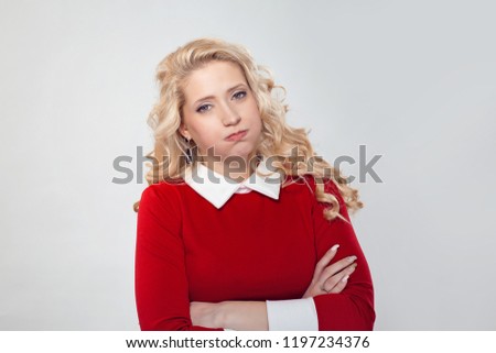Beautiful blond woman standing with arms crossed and puffing cheeks in boredom