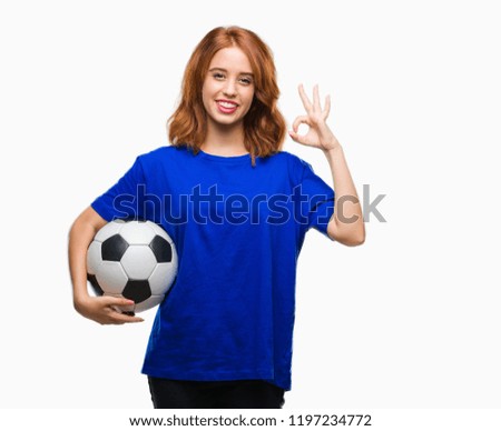Young beautiful woman over isolated background holding soccer football ball doing ok sign with fingers, excellent symbol