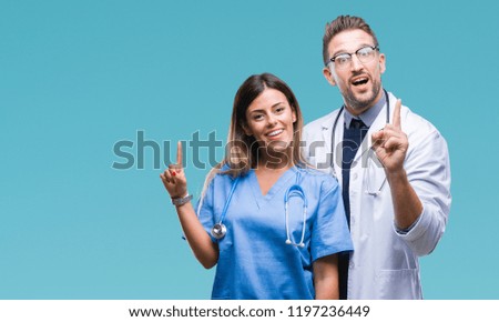 Young couple of doctor and surgeon over isolated background pointing finger up with successful idea. Exited and happy. Number one.