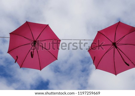 View from below of rows of pink hanging umbrellas in a french street. Pattern of similar decorative objects. Suuny day and blue cloudy sky in background. Artistic and abstract picture.  