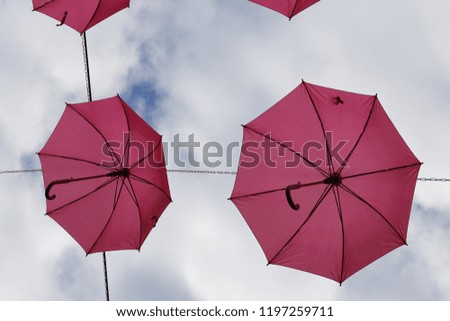 View from below of rows of pink hanging umbrellas in a french street. Pattern of similar decorative objects. Suuny day and blue cloudy sky in background. Artistic and abstract picture.  