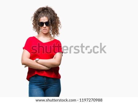 Beautiful brunette curly hair young girl wearing sunglasses over isolated background skeptic and nervous, disapproving expression on face with crossed arms. Negative person.