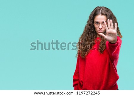 Beautiful brunette curly hair young girl wearing glasses and winter sweater over isolated background doing stop sing with palm of the hand. Warning expression with negative and serious gesture 